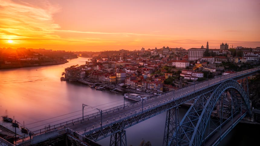 View of Porto during sunset hour showing the river, the rail bridge and part of the town. Image by Everaldo Coelho on Unsplash.