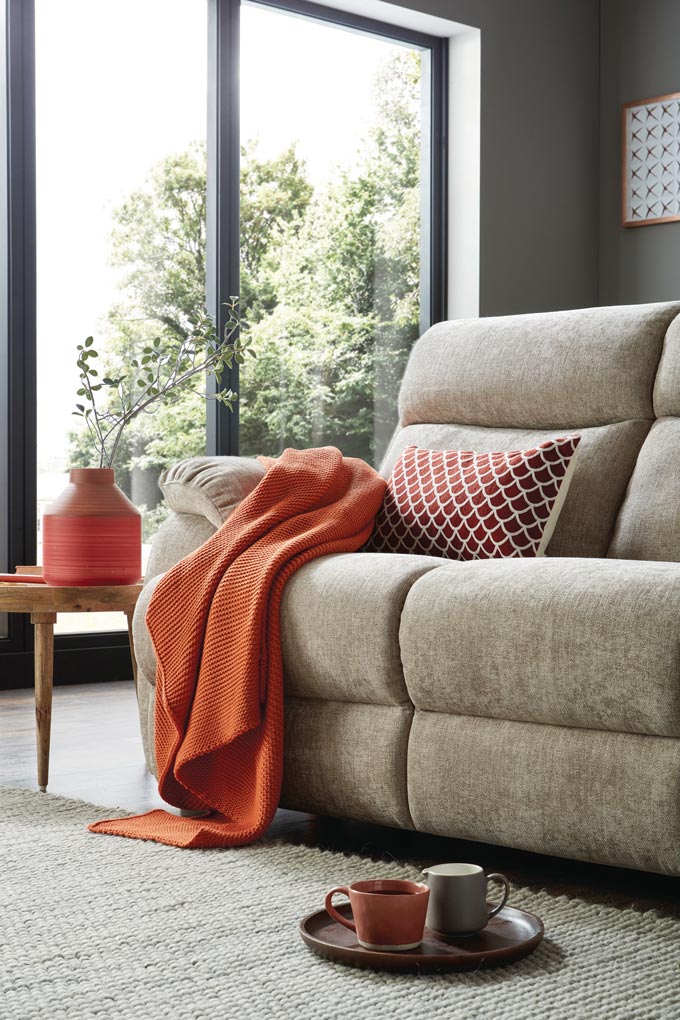 A soft grey sofa coordinated with a soft grey neutral area rug in a room flooded with natural light. Via Sofology. Soft furnishings: tips for renters you should know about.