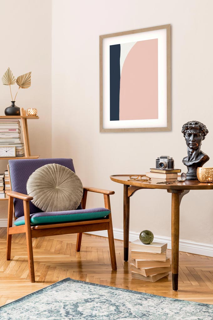 A Mid Century inspired vignette featuring an armchair, table, decor and an abstract art print on the wall. Via Abstract House.