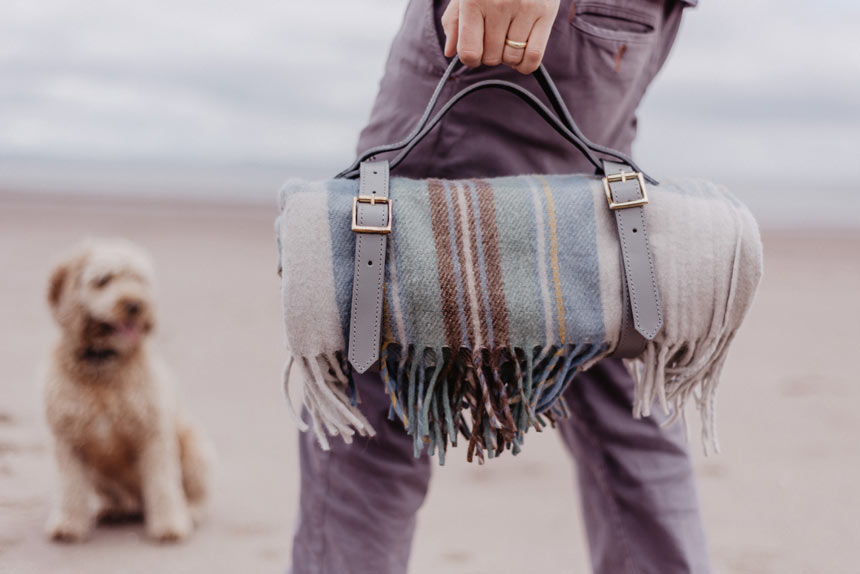 A man carrying a picnic blanket with a leather strap made of recycled wool. Via Tartan Blanket Co.