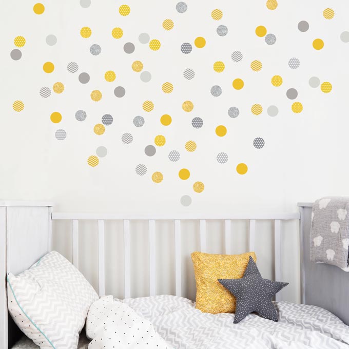 A cot bed against a white wall decorated with yellow and gray polka dot wall stickedrs. Via Koko Kids.