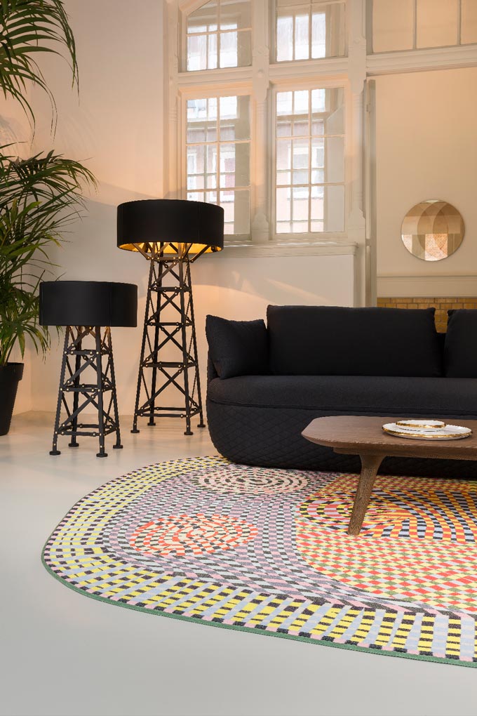 A styled corner of a living room with a black sofa, two floor lamps with black shades, but a muted colorful patterned area rug by Moooi Carpets. Via Nest.co.uk.