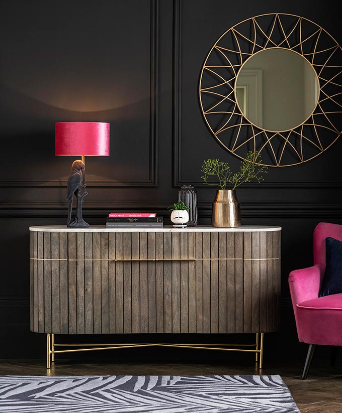 A moody interior with a beautiful sideboard vignette and a pink velvet armchair on the side that pops. Image via Next.