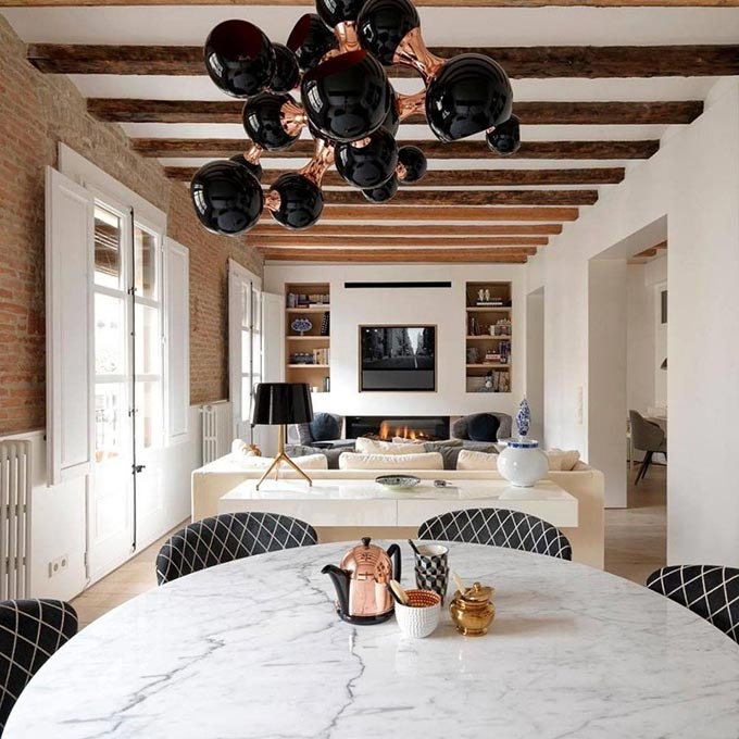 A beautiful dining room in the foreground and a living room with a fireplace in the background and exposed wooden beams across the entire ceiling. Image: DelightFULL.