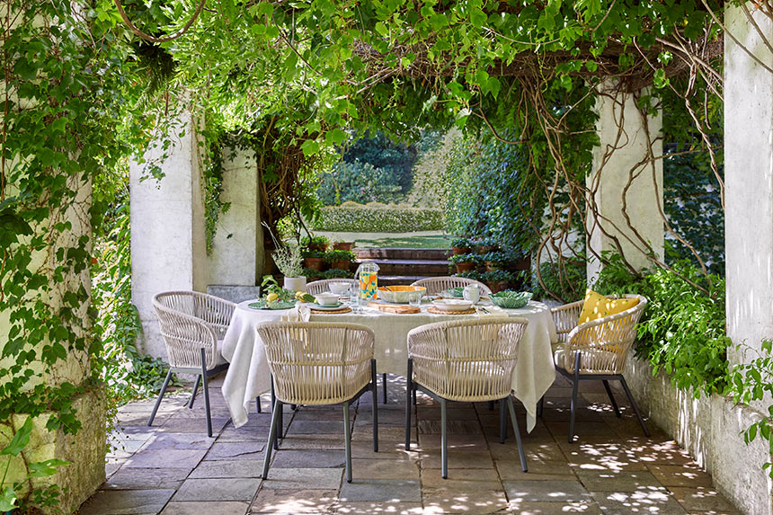 A beautiful stylish outdoor dining setup in a garden with English ivy and other plants forming a canopy. Image: John Lewis.