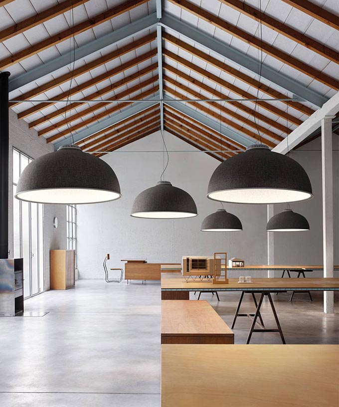 A minimal open plan working space with an accent ceiling due to the exposed steel and wooden beams and hanging pendant lights. Image: Luceplan by Diego Sferrazza.