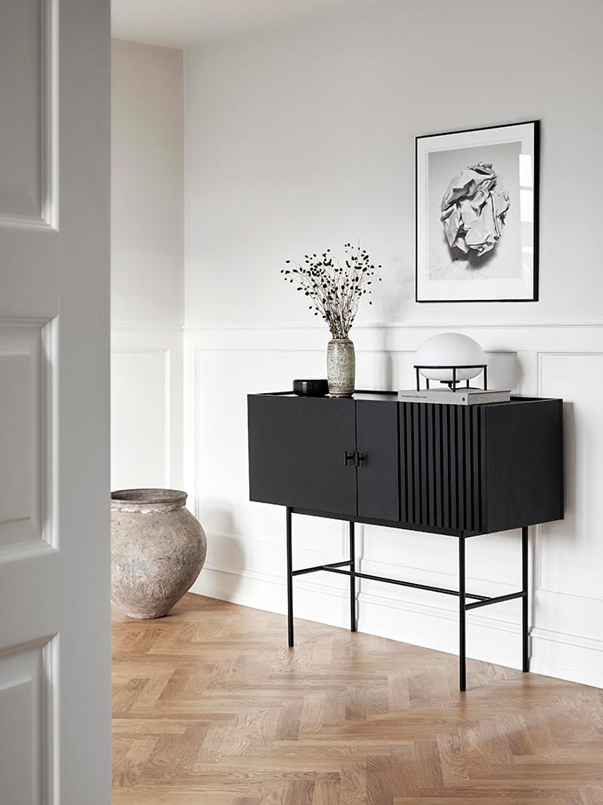 A minimal black sideboard against a wall with wainscotting and an black and white artprint over it. The Woud Pump table lamp is featured. Image: Nest.co.uk.