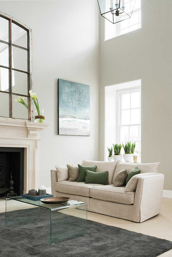 A stylish, bright living room with a double height ceiling, a fireplace styled with an oversized mirror and a beautiful 3 seater sofa. Image: Collins & Hayes.