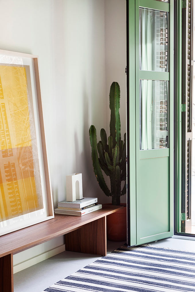 Detail view of an open window door with a bench besides on stacked with art prints and books. Image: Elton Rocha for Culto.