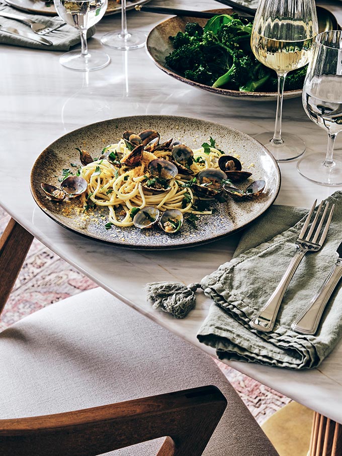 The perfect dish for a dinner party. A close up over a dinner plate with pasta and mussels placed on a mable dining table. Via: Soho House Retail.