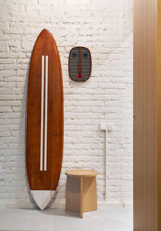 A surf board, a stool and a tribal like mask hanging pose as the entryway decor in a small apartment in Barcelona. Image: Elton Rocha for Culto.