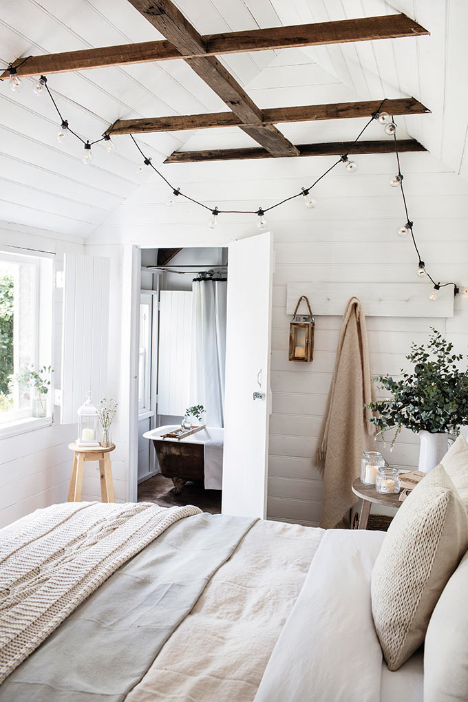 A white, bright bedroom with a rustic vibe and a string of lights hanging from the wooden beams of the pitched roof. Image: Lights4fun.