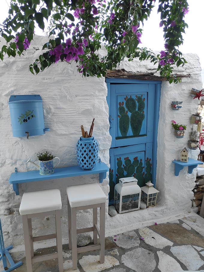 A whitewashed building facade with a blue door and cacti painted on it, in Ano Syros.
