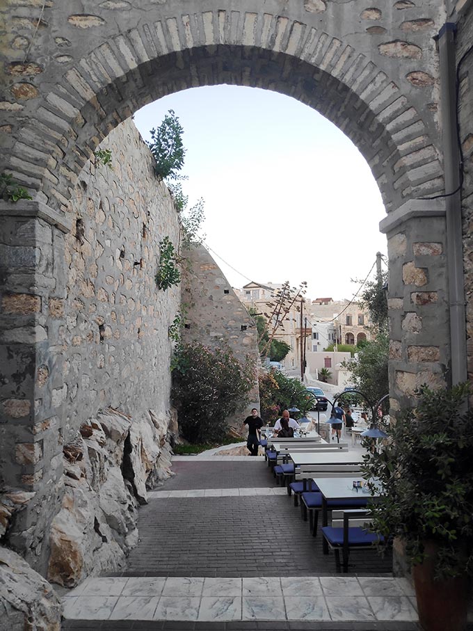 An masonry archway in Hermoupolis with outdoor dining setups Sta Vaporia.