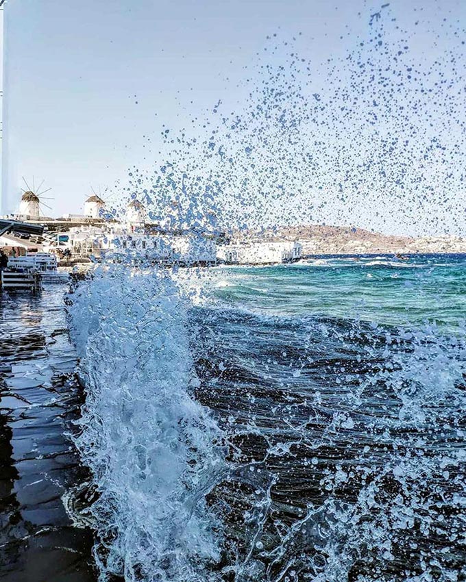 Detail view of the splashes and waves that break at Little Venice in Mykonos with the windmills in the background.