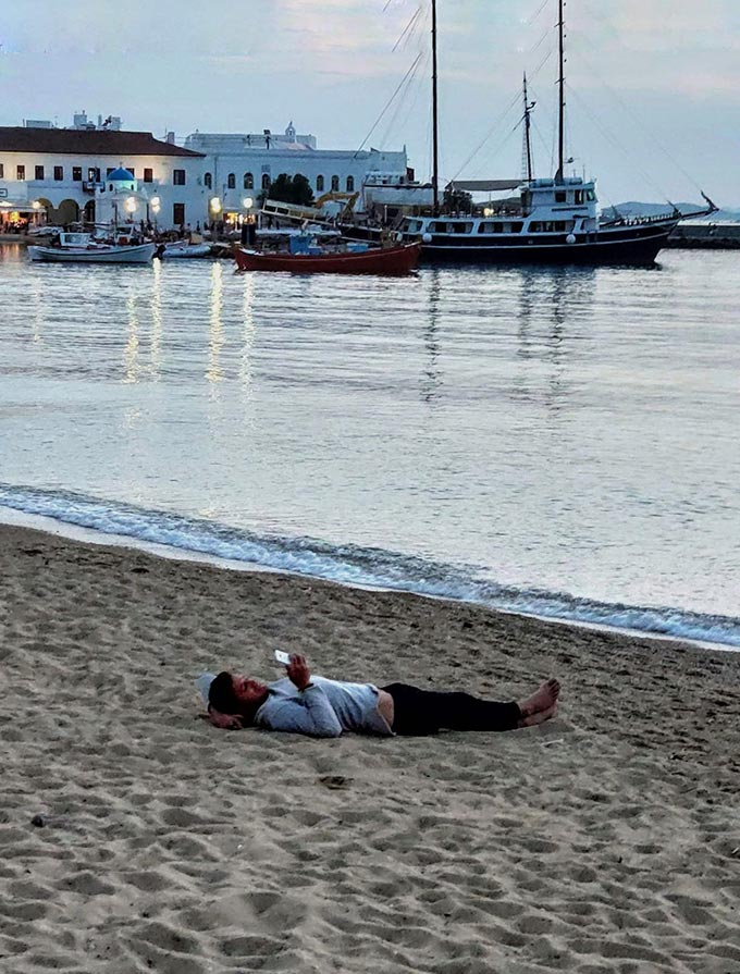 A man lying on a sandy beach in Chora, Mykonos.