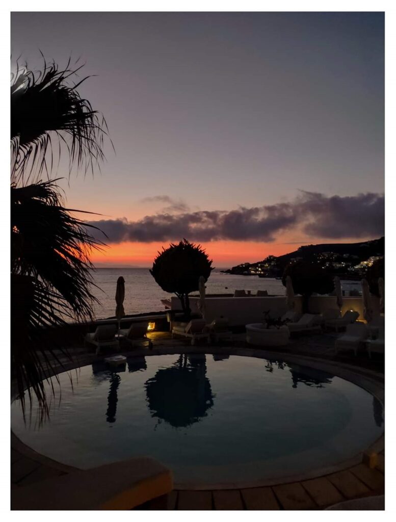 View of a round pool in the foreground and the sea front in Mykonos after sunset.