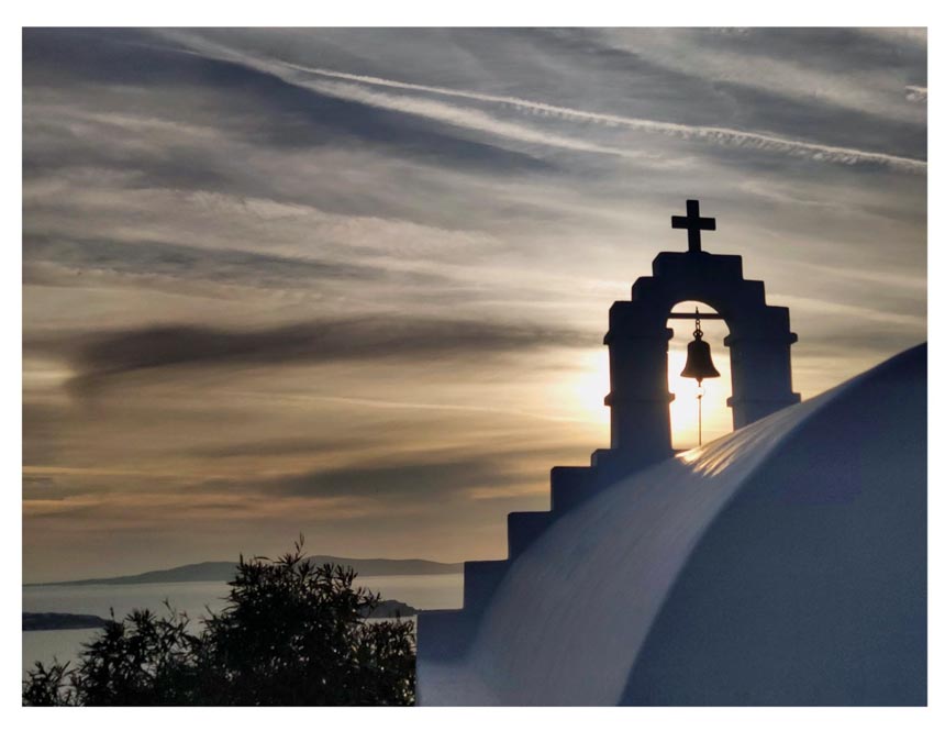 View of sea in the background and a chapel's bell tower in the foreground partially hiding the evening's sun.