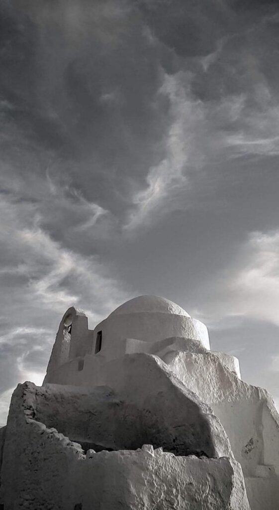 A white washed chapel against a moody cloudy sky.