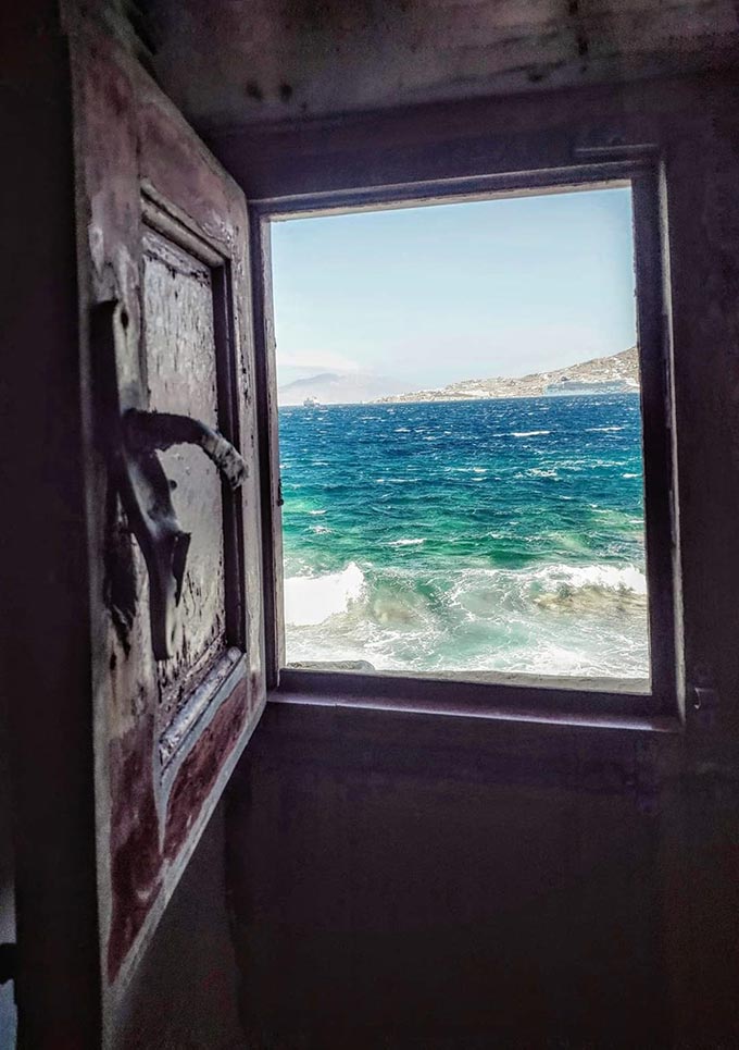 An open old window that overlooks a rough sea in Mykonos.