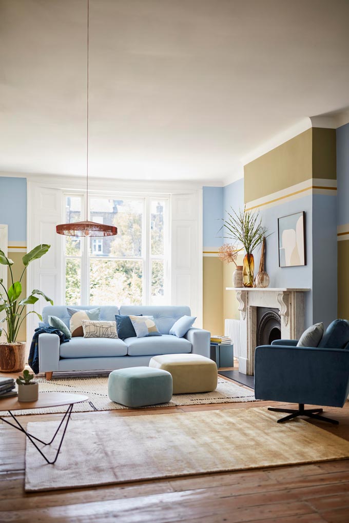 A contemporary living room with color blocked walls, a four seater sofa in Dulux's Color of the Year 2022 Bright Skies, a swivel chair and a fireplace. Image: DFS CO. PLC.