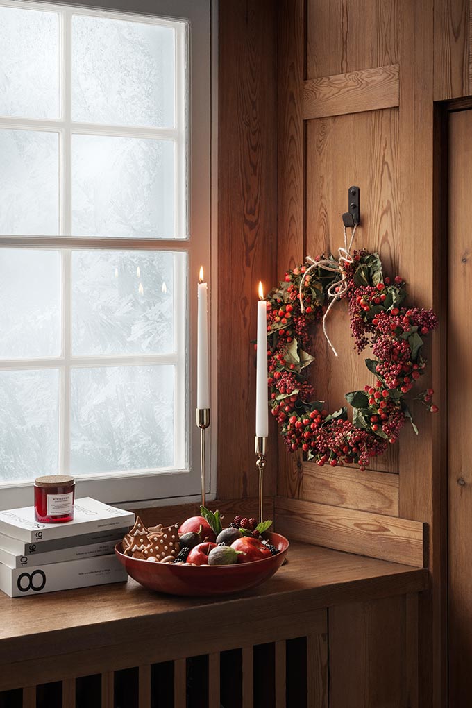A beautiful Christmas wreath with holly berries hanging near a window, besides other Christmas decor. Image: H&M Home.