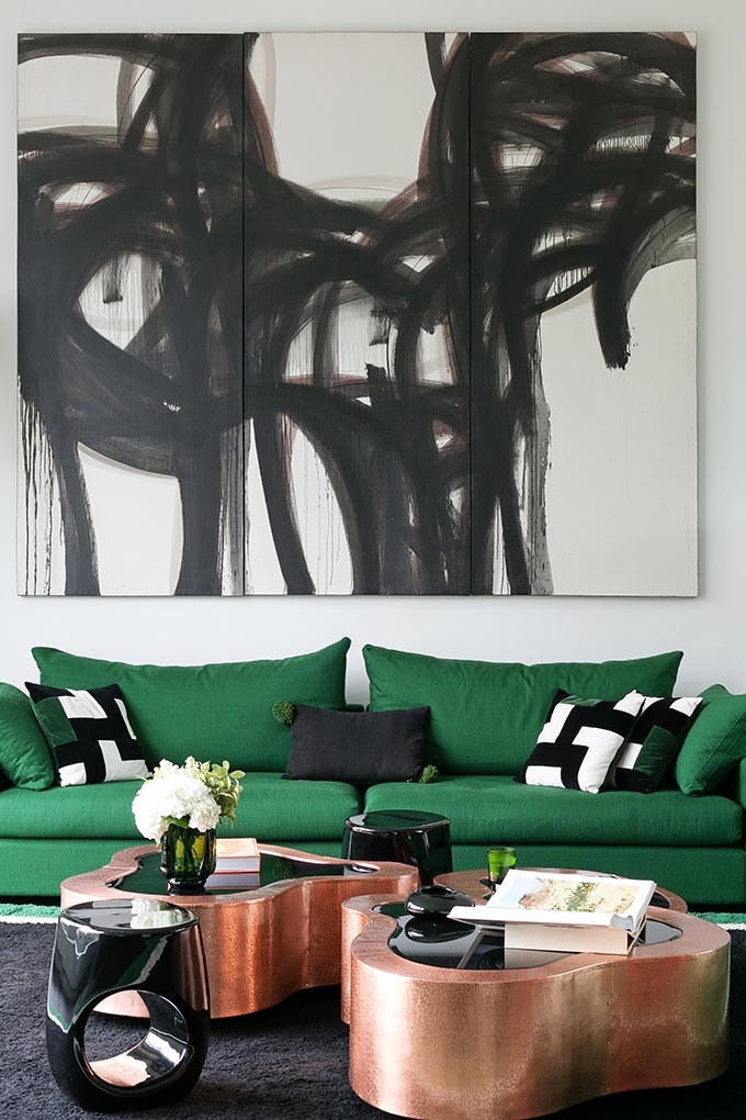 A bold sitting room from a Parisian apartment, with a green sofa and an abstract painting atop, featuring two curvy copper metal coffee tables. Image: Boca do Lobo.