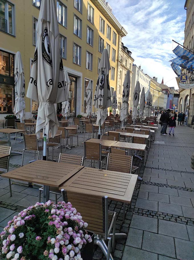 Partial view of a pedestrian zone with some high end stores and many outdoor dining setups at the center of Munich.