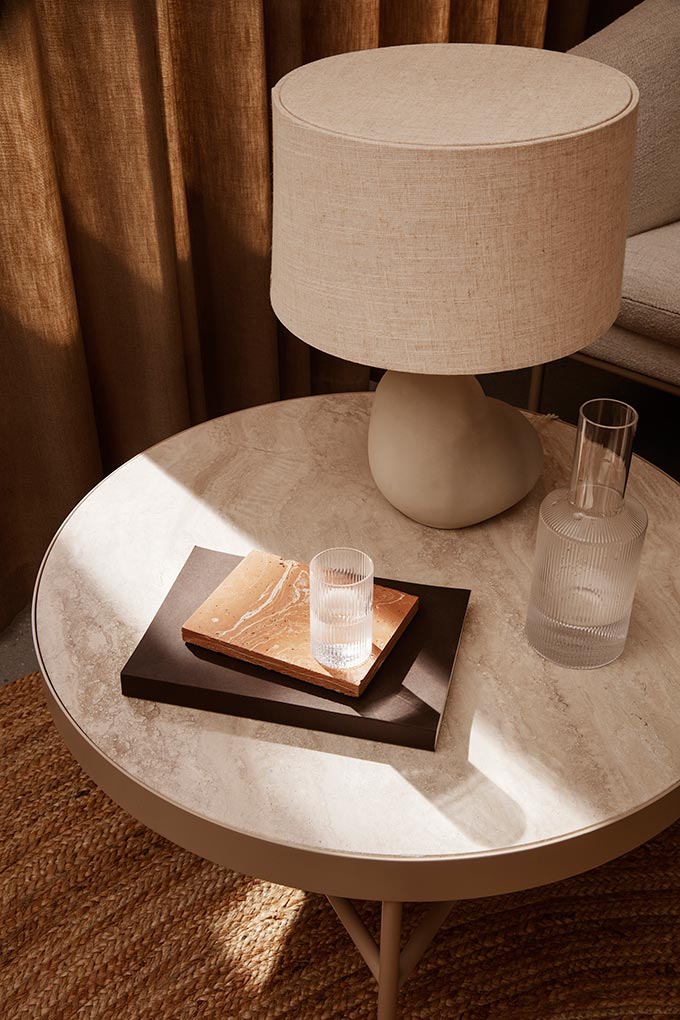 A Scandi warm minimalist vignette featuring a round side table with a curvy table lamp. Image: fermLIVING.