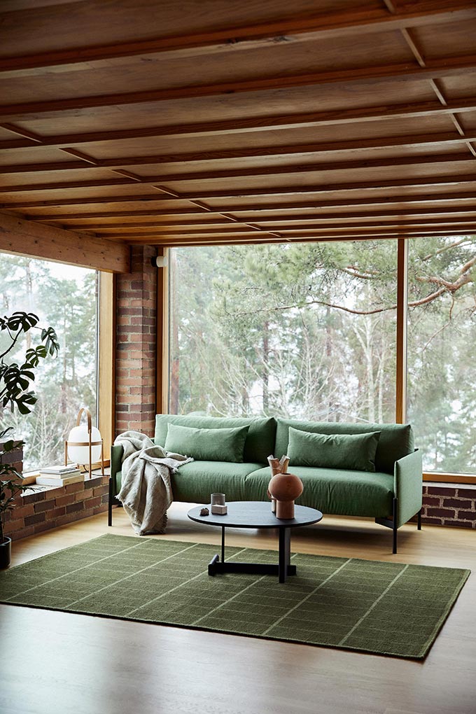 A contemporary sitting room with a green sofa, a green Ribbon Rug, and large windows lending view to a snowy landscape. Image: Nest.co.uk.
