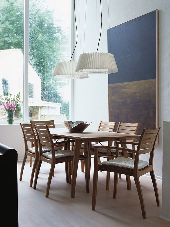 A stylish dining area with a large window in the background, a large artwork on the wall and the Ballare chairs from Skagerak. Image: HolzDesignPur.