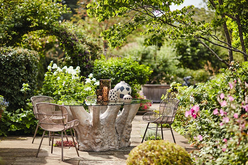 A beautiful dining setting in the middle of a wild garden, where the table featured is a tree trunk. Image: OKA UK.