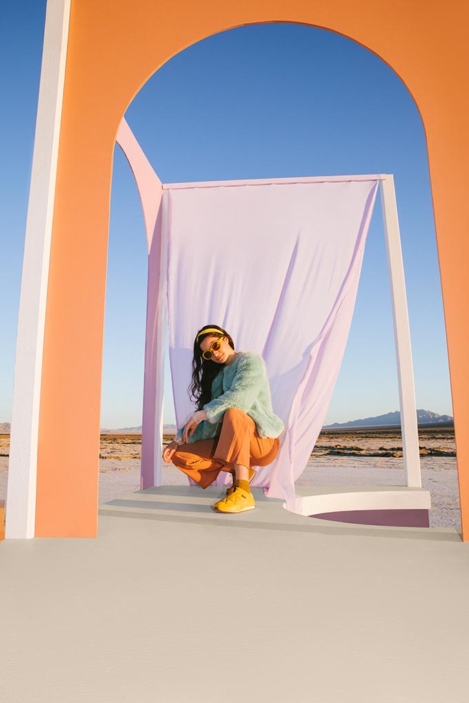 A lifestyle image of woman dressed in yellow Teva trainers, orange pants and cyan jacket. Image: TEVA.