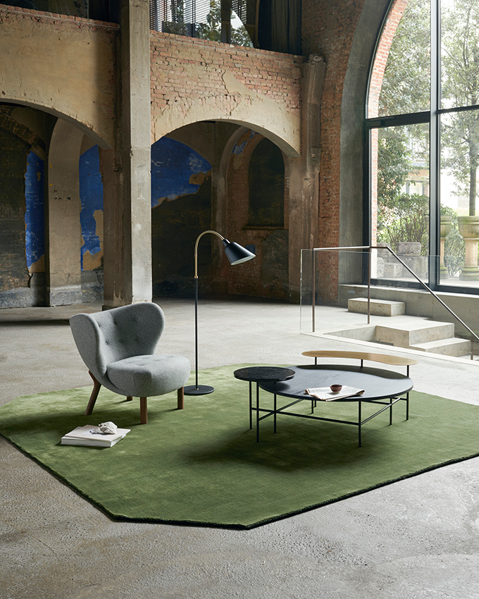 A lifestyle shot of an industrial interior with a green area rug, a grey armchair and the Palette JH25 Coffee Table. Image: &Tradition.