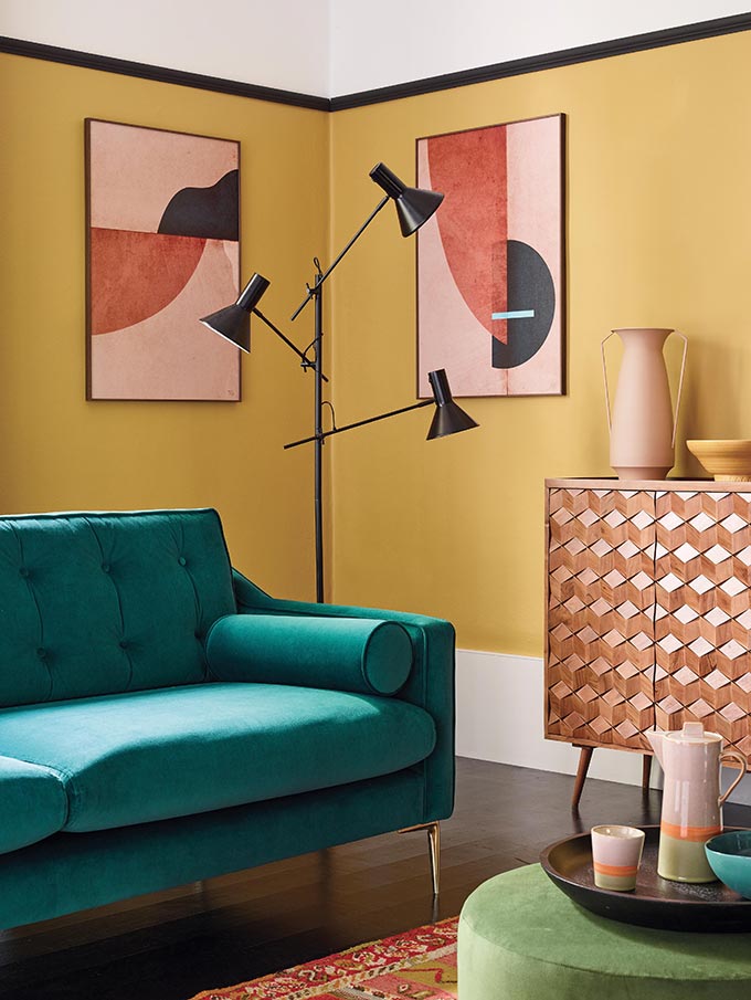 A lifestyle image of a sitting room with yellow ochre walls, the Swoon Rene sofa in teal velvet and a black floor lamp. Image: DFS.co.uk.