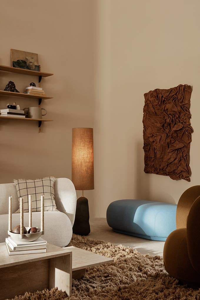 A lifestyle image of an eclectic Nordic sitting room in warm terracotta hues featuring a curvy white sofa and a tiered travertine coffee table - Distinct. Image: fermLIVING.