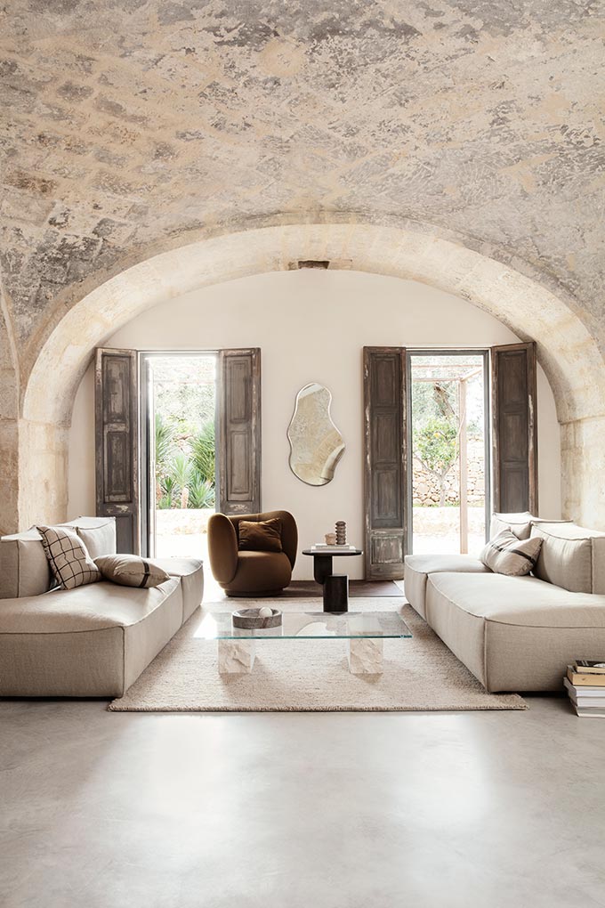 A lifestyle image of an off white sitting room featuring to comfy sofas, a brown curvy armchair and the Mineral Coffee table. Image: fermLIVING.