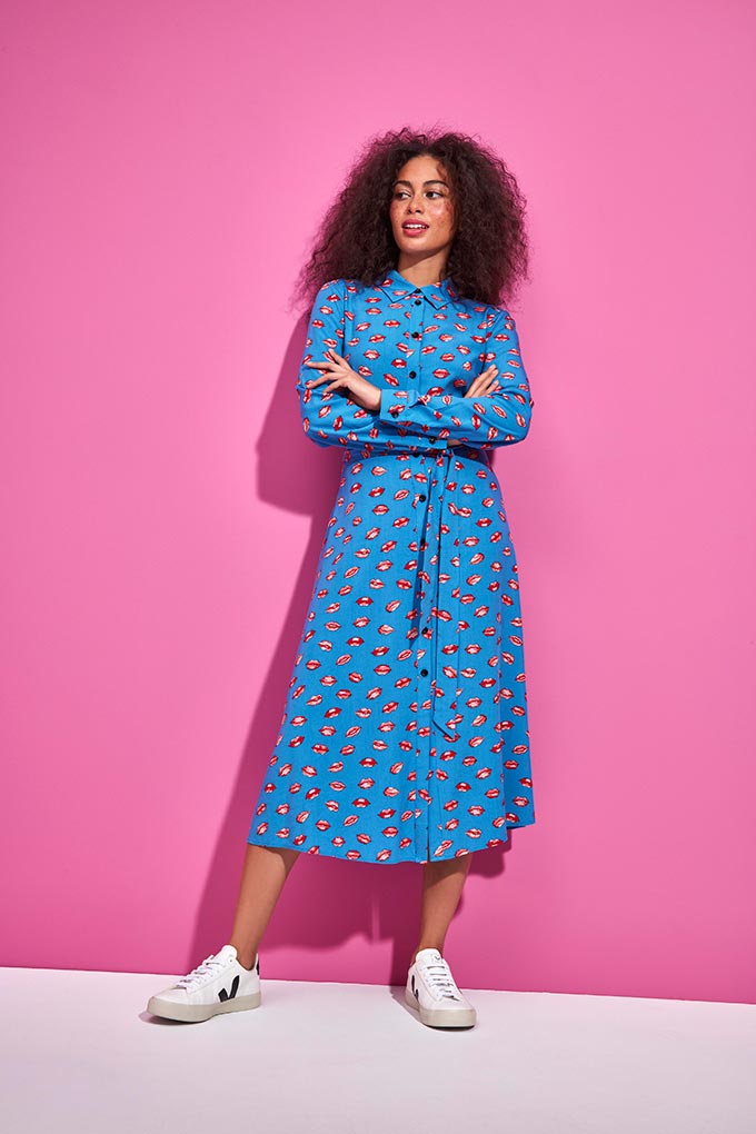 A woman dressed in Veja trainers and a blue dress with a red lips print. Image: M&Co.