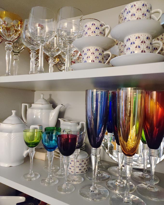 Shelves stacked with colored glasses in various sizes, colors and shapes and other various porcelain-ware.