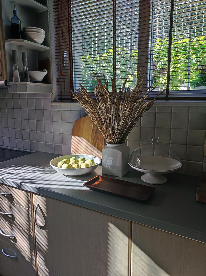 Partial view of a kitchen with a window covered in wooden Venetian blinds. Image by Velvet Karatzas.