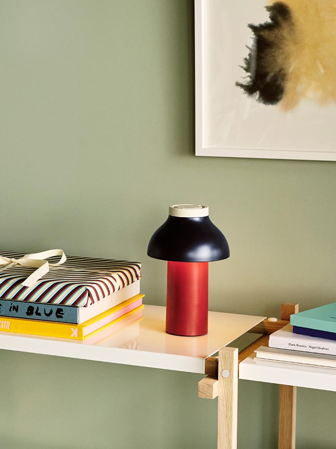 A lifestyle image of the HAY PC portable lamp on a shelf next to a stack of books. Image: Nest.co.uk.