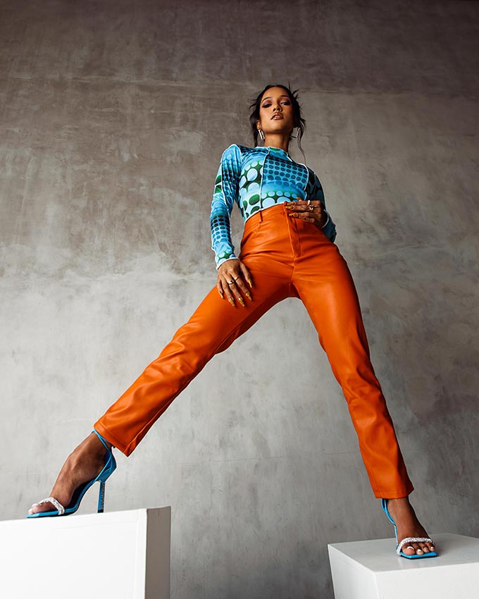 A lifestyle image of a woman in orange faux leather pants and a blue top. Image: PrettyLittleThing.