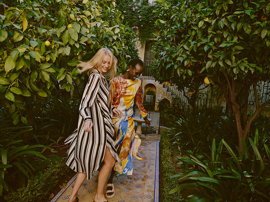 A lifestyle image of two women dressed in spring dresses. Dopamine dressing isn't just about colors. Image: River Island.