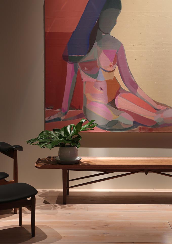 A lifestyle image of a House of Finn Juhl Cocktail bench under a large abstract painting of a woman. Image: Nest.co.uk.