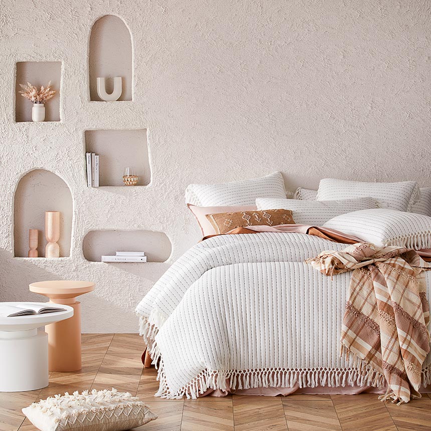 A warm minimal off white and muted terracotta toned bedroom with a textured accent wall and alcoves and off white ridged bedlinen from Adairs. Image: Adairs.