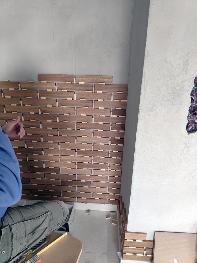 A man installing oak tiles on a faux concrete wall during an installation. Image: Velvet Karatzas.