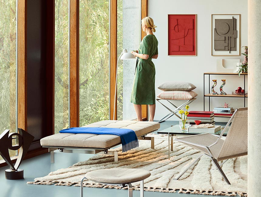 Lifestyle image of a living room with floor to ceiling windows with a modern vibe and a blonde lady looking out, featuring the Fritz Hansen PK