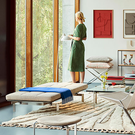 Lifestyle image of a living room with floor to ceiling windows with a modern vibe and a blonde lady looking out, featuring the Fritz Hansen PK25 chair. Image: Nest.co.uk