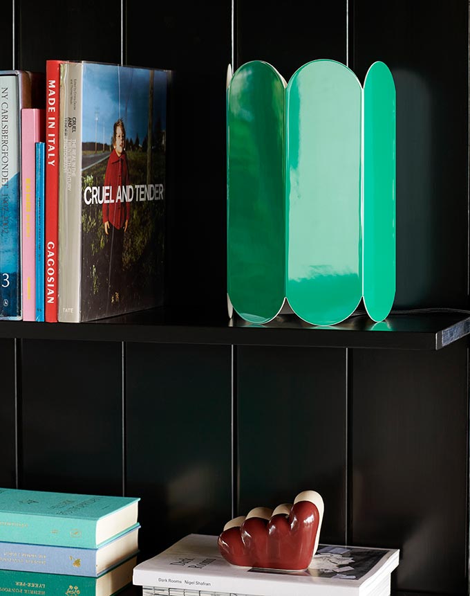 A lifestyle image close up of a black bookcase with books and the green Arcs table lamp from HAY. Image: Nest.co.uk.