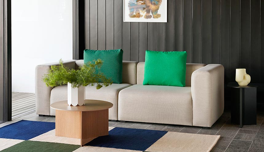 Lifestyle image of a sitting room with an off white sofa, green throw pillows and the round HAY Slit coffee table. Image: Nest.co.uk.